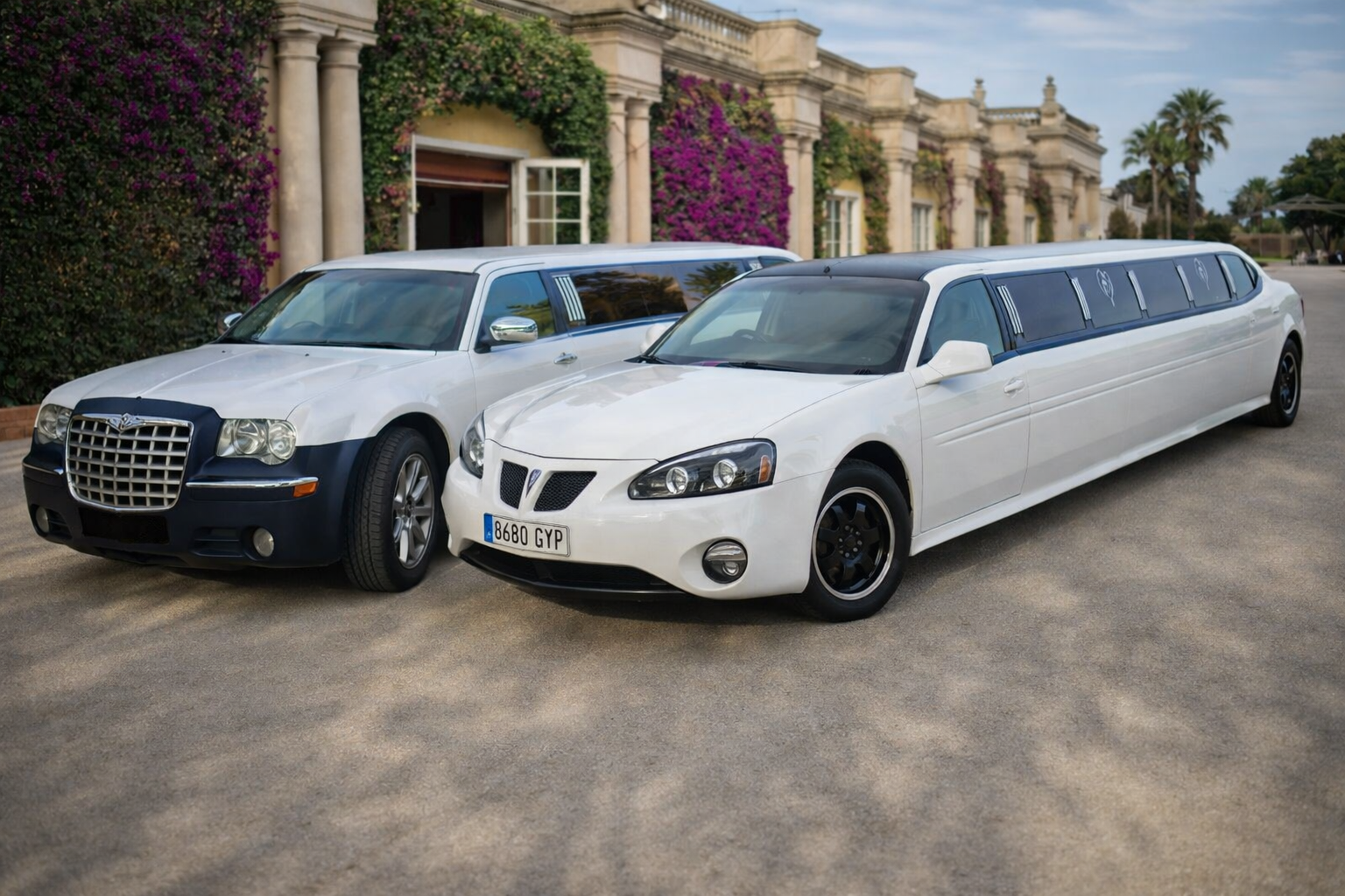 Limos frente a una mansión mediterránea "Dos limusinas blancas estacionadas juntas frente a una elegante mansión de estilo mediterráneo con columnas y buganvillas rosas, en una fotografía realista tomada a plena luz del día.