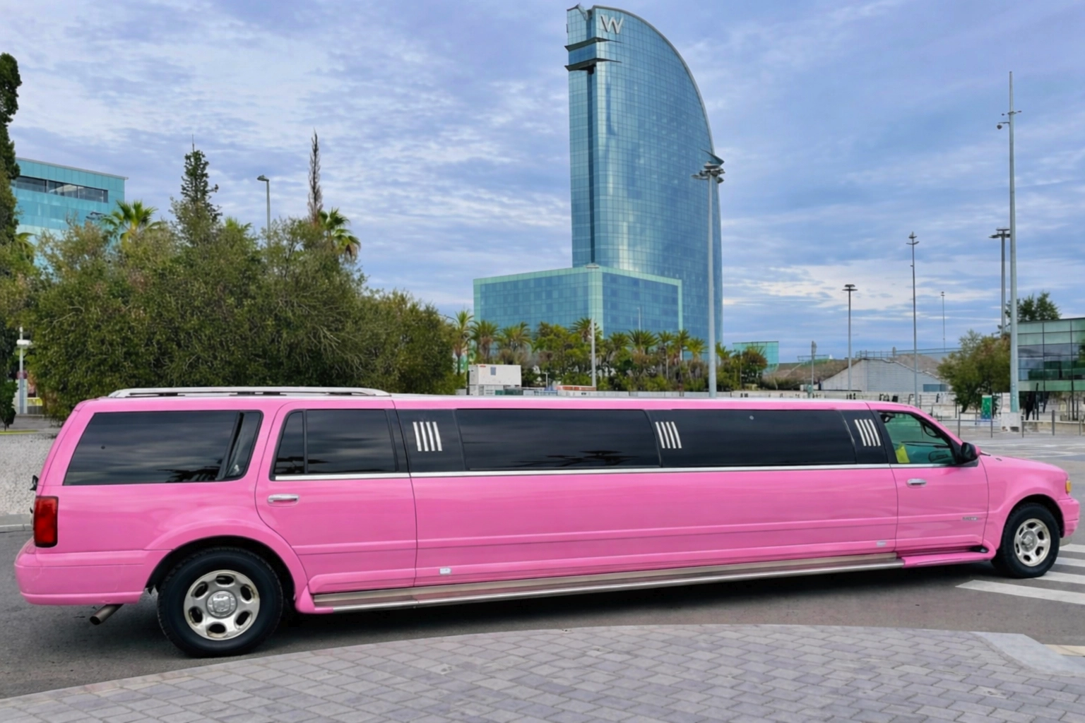 limusina rosa Hummer fondo hotel w Limusina rosa en Barcelona con el Hotel Vela de fondo, destacando su estilo llamativo y elegante en un entorno urbano icónico.